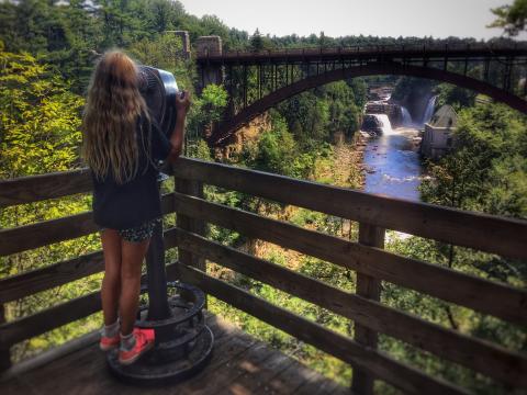 A girl uses binoculars to view a waterfall
